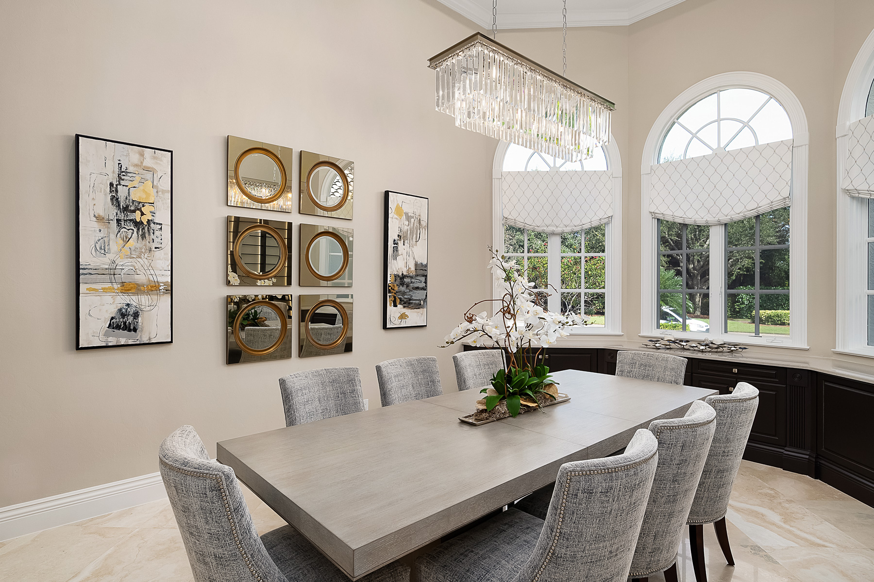 Formal dining room has a contemporary crystal chandelier and decorative gold mirrors overlook a long grey wash table with seating for eight in casually elegant chairs